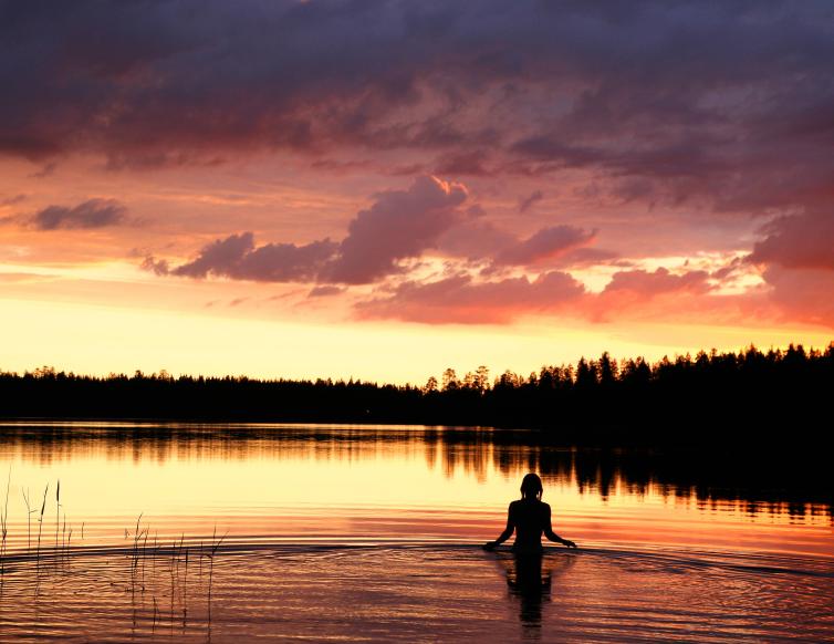 Ihminen katsomassa keskiyön auringon valaisemaa järvimaisemaa