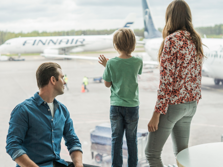 Family watching aeroplane from window in terminal.